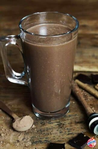 a glass mug filled with chocolate on top of a wooden table next to spoons