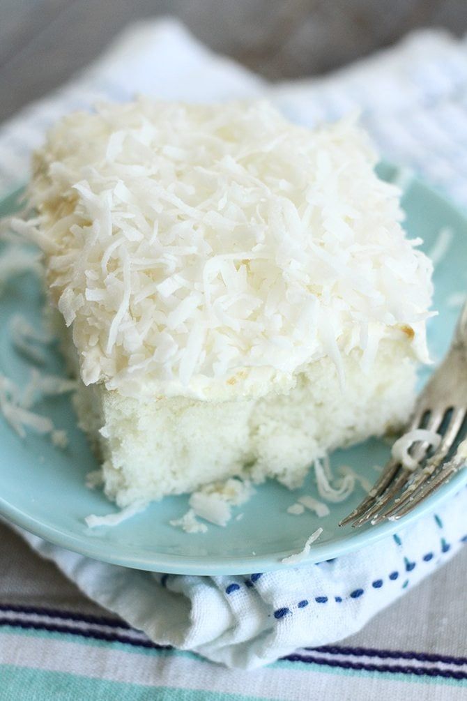 a piece of coconut cake on a blue plate with a fork and napkin next to it