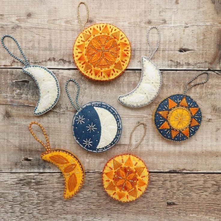 four ornaments are hanging on a wooden surface, each decorated with an orange and blue moon