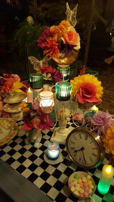 a table topped with lots of different types of flowers next to an alarm clock and candles