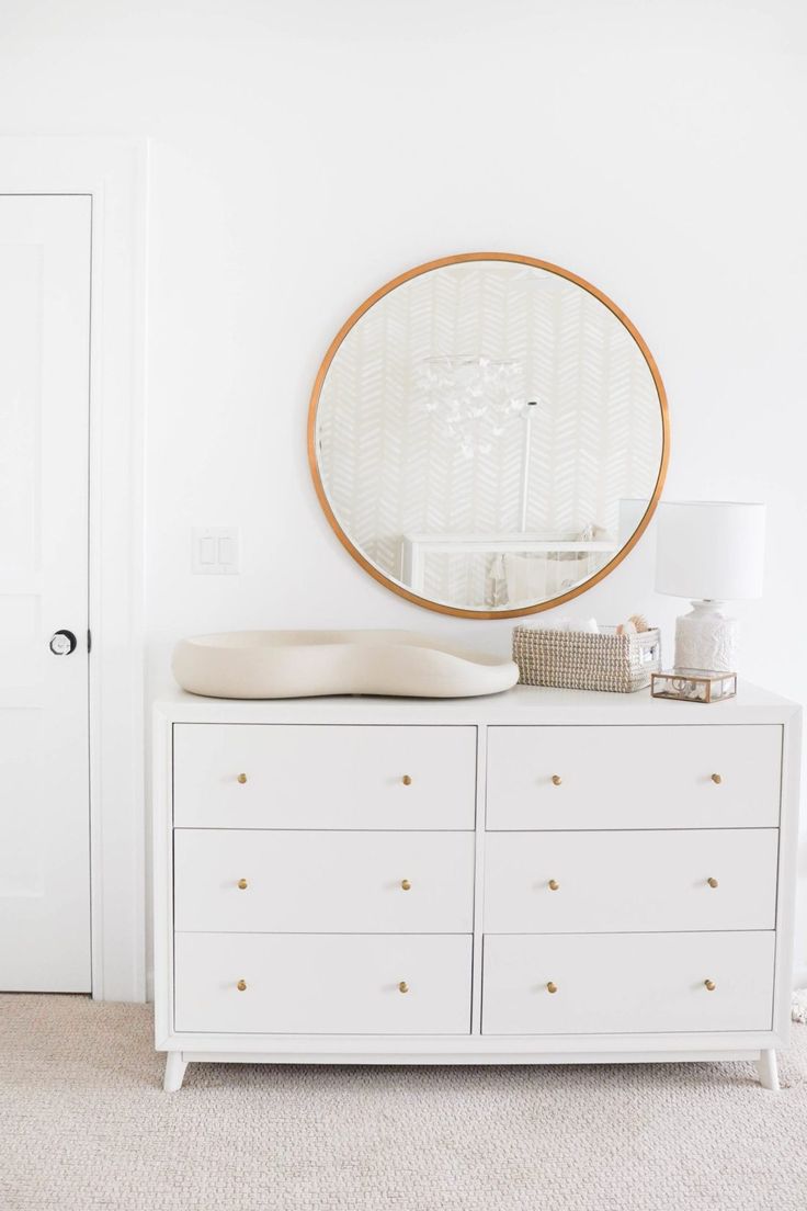 a white dresser with a round mirror above it