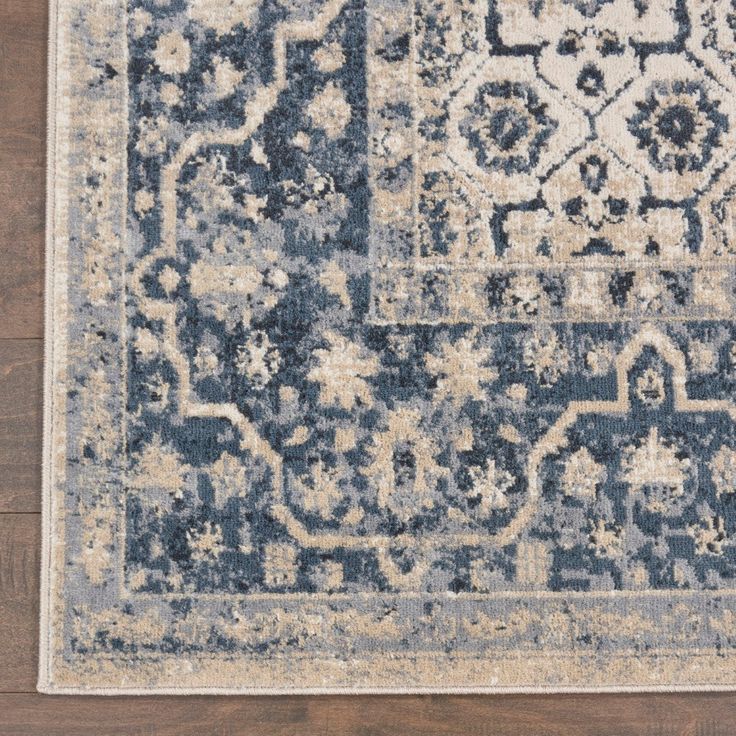 a blue and beige area rug with an ornate design on the center, in front of a wooden floor