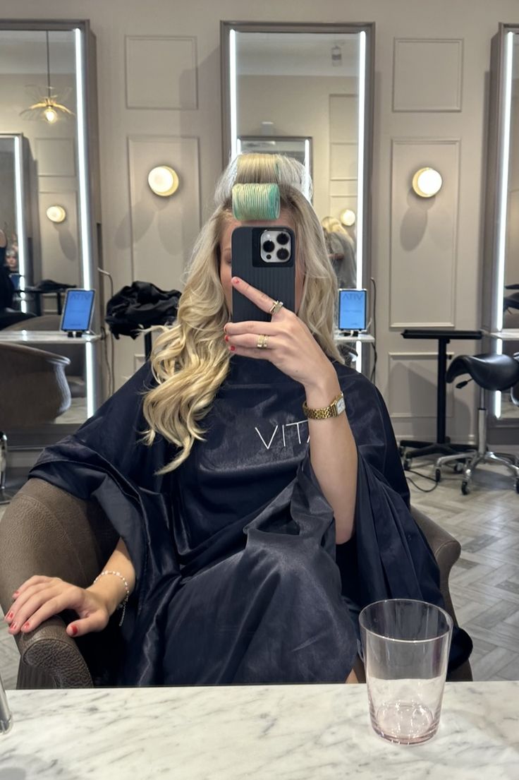 a woman sitting in a chair taking a selfie with her cell phone while she is getting her hair done