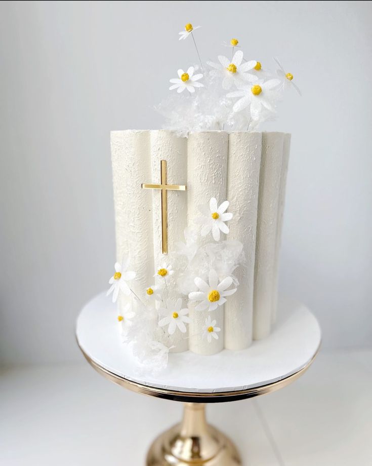 a cake decorated with white flowers and a cross on top is sitting on a gold plate