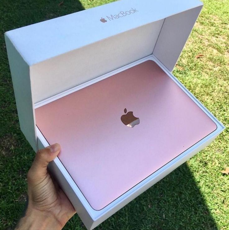 someone holding an apple macbook pro in their hand, with the box open on grass