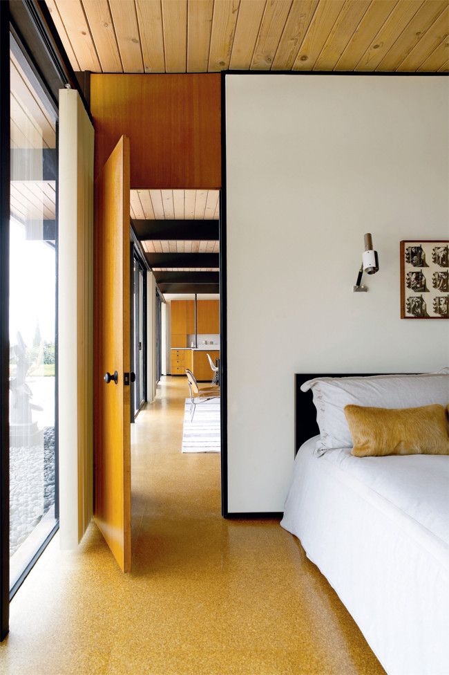 a bedroom with white bedding and wooden ceilinging next to a sliding glass door