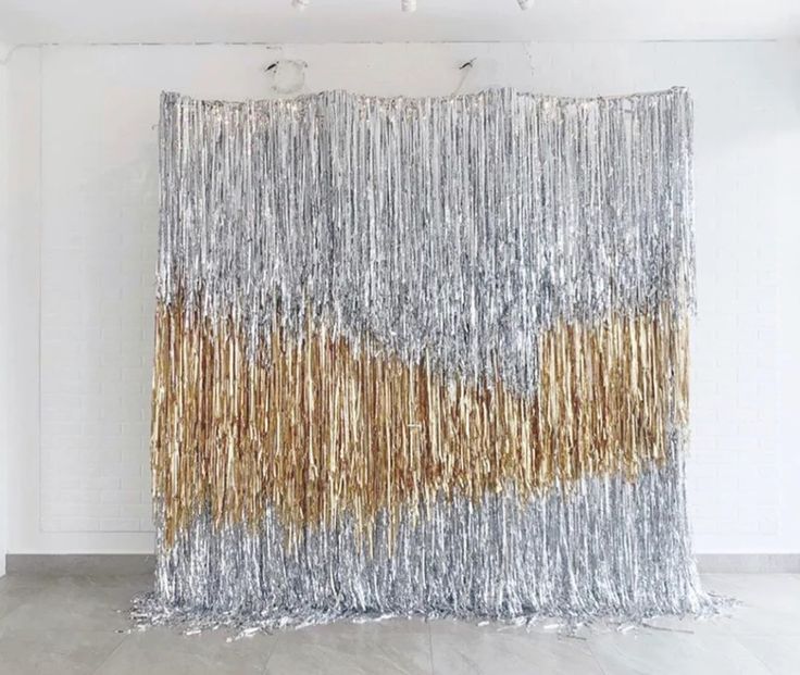 a large silver and gold foil curtain hanging from the ceiling in front of a white wall