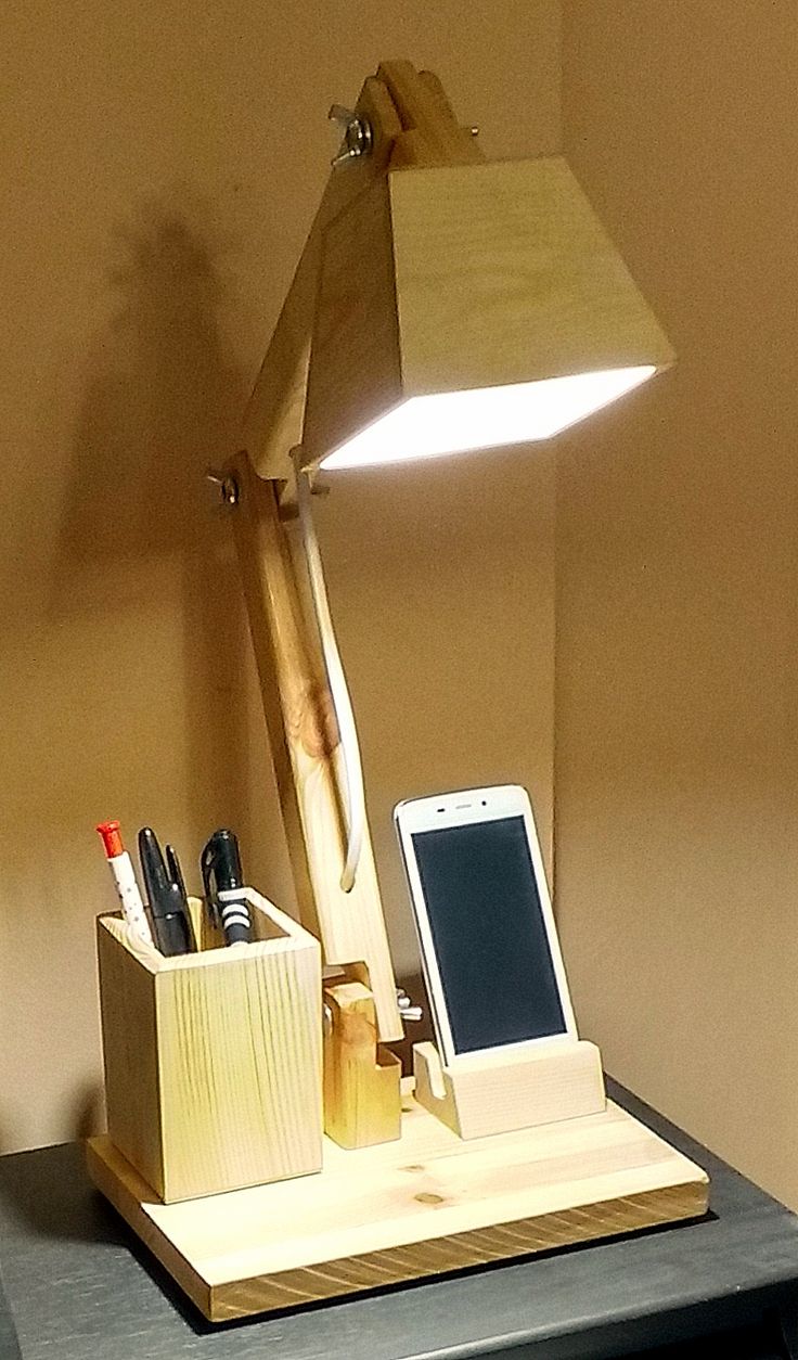 a wooden desk lamp sitting on top of a table next to a cell phone and pen holder