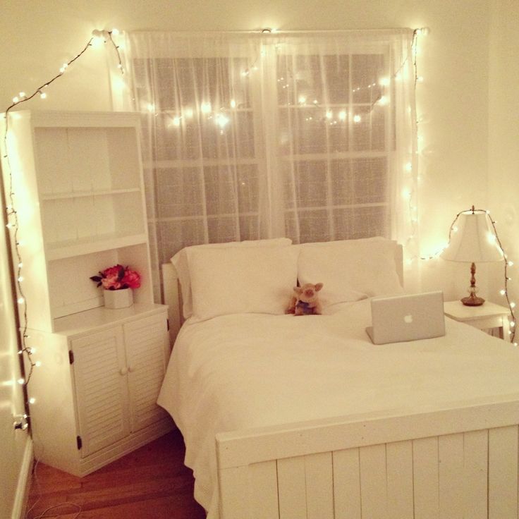 a bedroom with white bedding and fairy lights