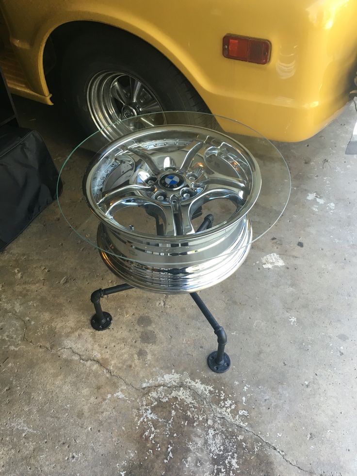 a glass table with wheels on it in front of a yellow car