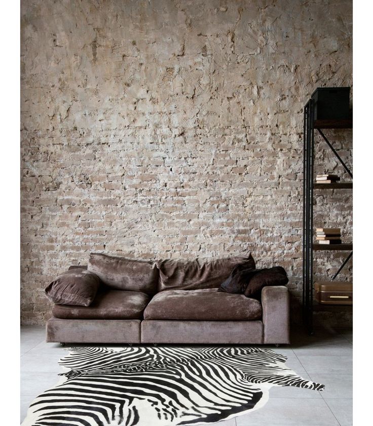 a zebra print rug in front of a brick wall with a sofa and shelving unit