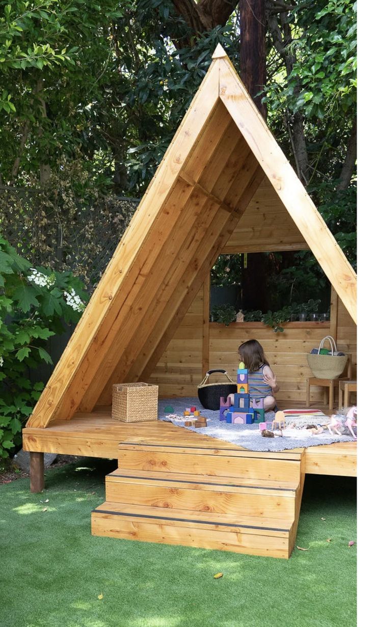 a child is sitting at a picnic table in a small wooden structure with stairs leading up to it