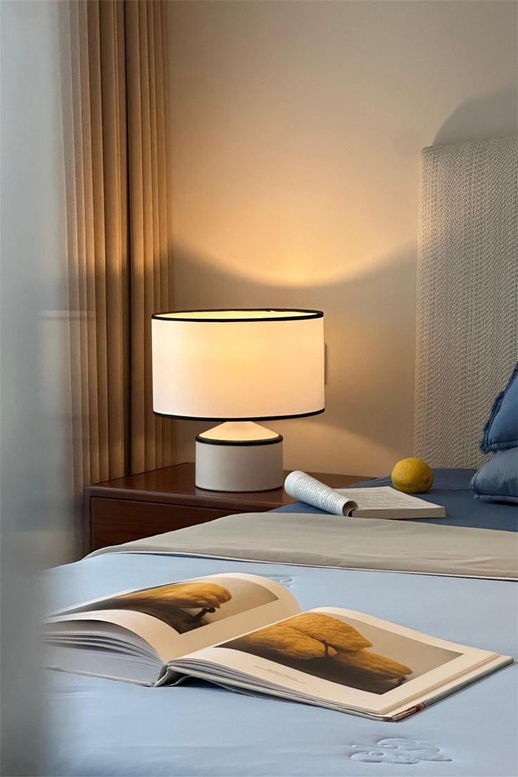 an open book sitting on top of a bed next to a lampshade and lamp