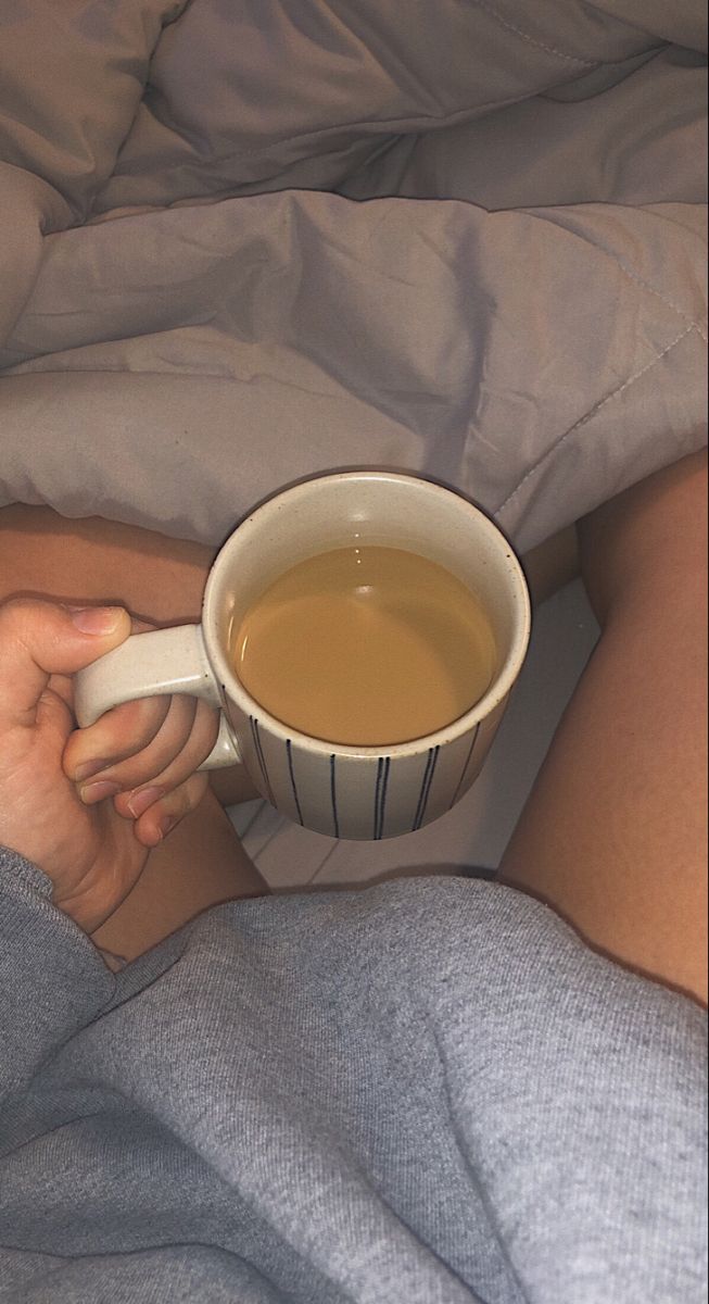 a woman laying in bed with her stomach wrapped around a cup of hot chocolate tea