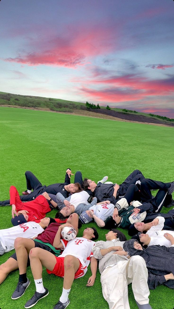 a group of young men laying on top of a lush green field next to each other