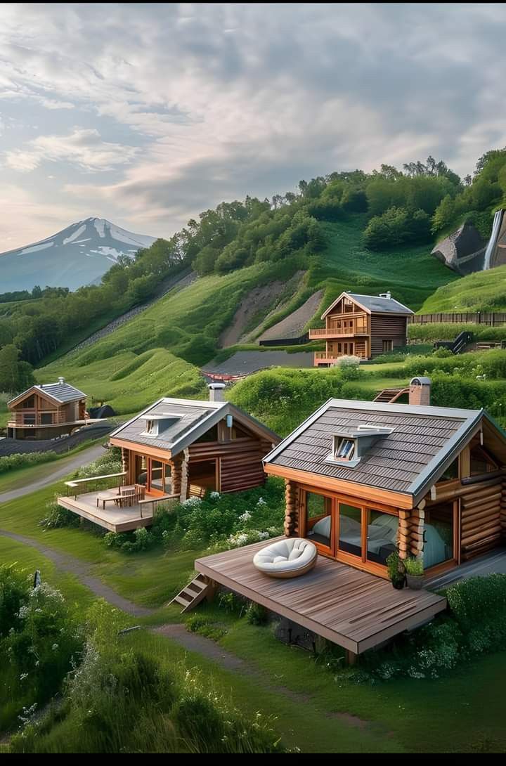 an artist's rendering of small wooden houses on a hillside with mountains in the background