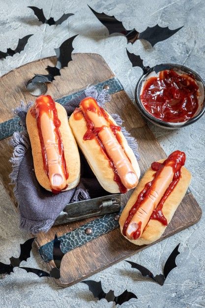 three hotdogs with ketchup on a cutting board next to a knife