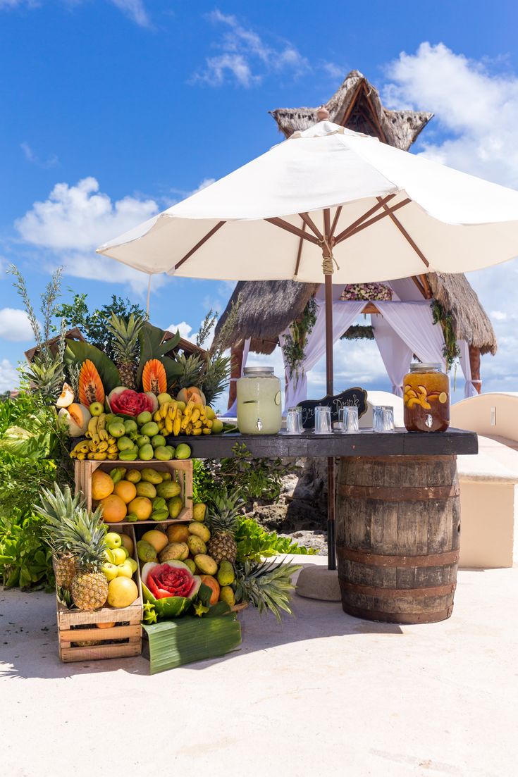 a table with fruits and drinks under an umbrella