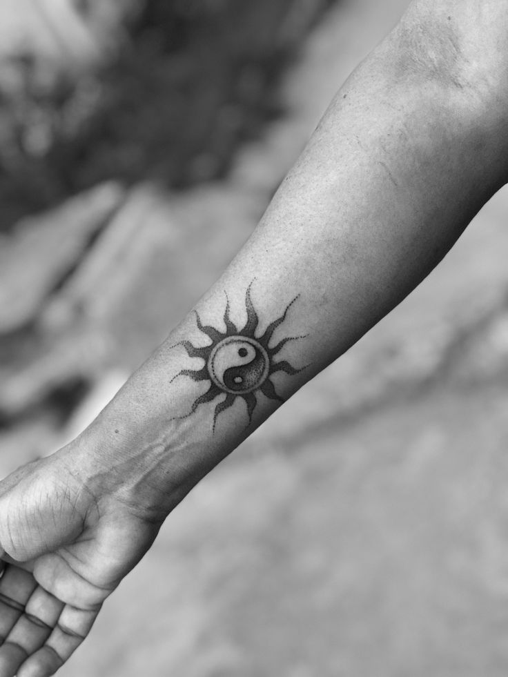 a black and white photo of a person's arm with a sun tattoo on it