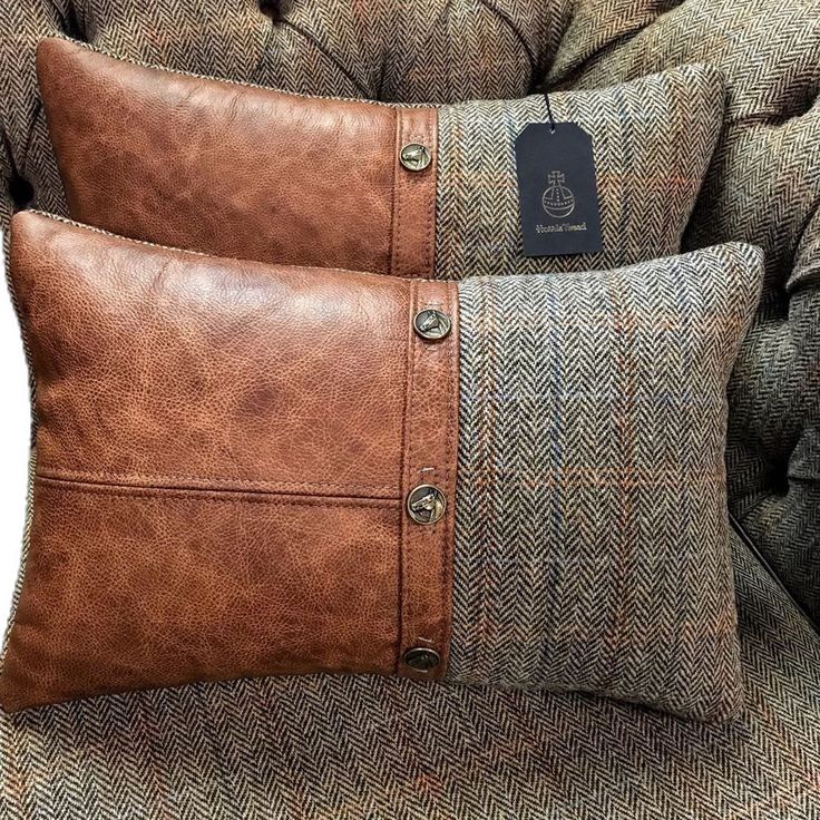 two brown leather pillows sitting on top of a gray couch next to a black tag