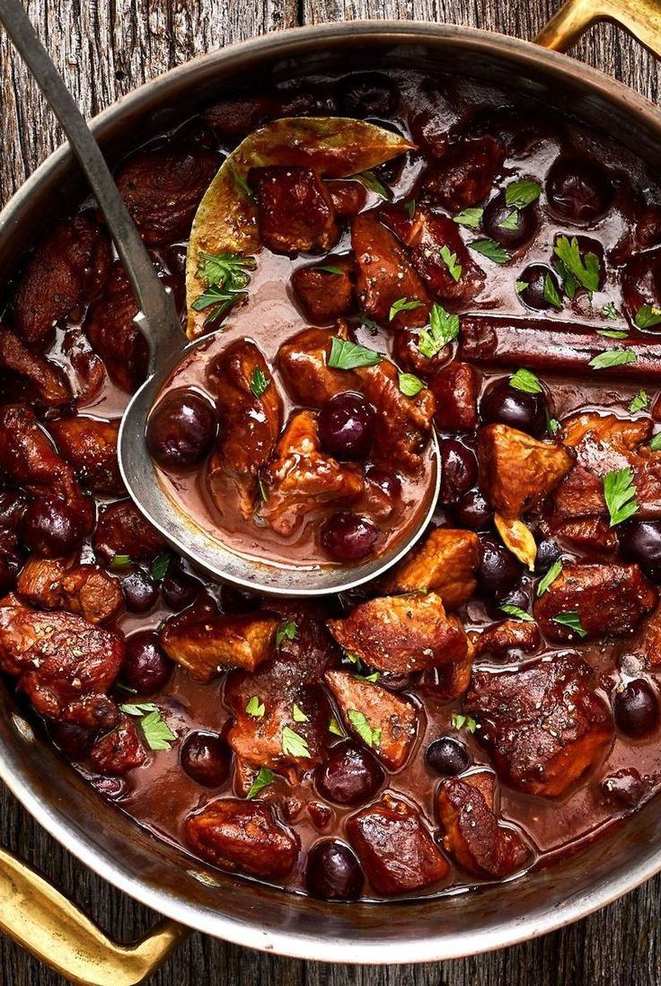 a pan filled with meat and olives on top of a wooden table