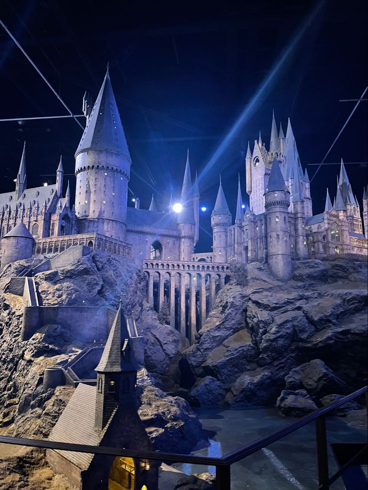 the hogwarts castle is lit up at night in front of a rock wall