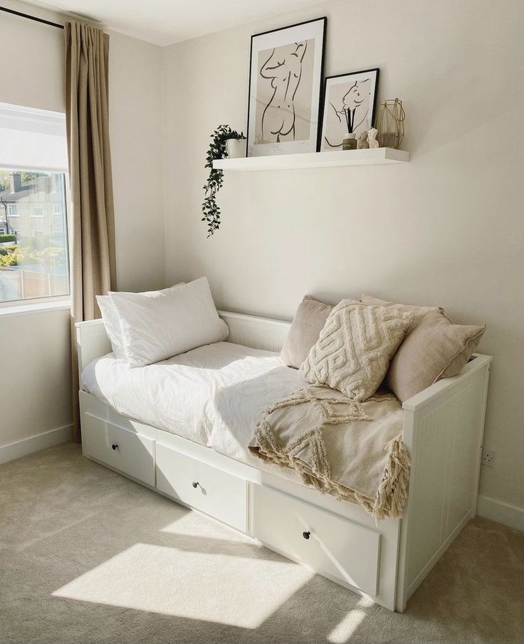 a white day bed sitting in a bedroom next to two framed pictures on the wall