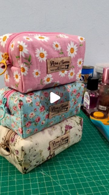 three cosmetic bags are stacked on top of each other, one is pink and the other has white daisies