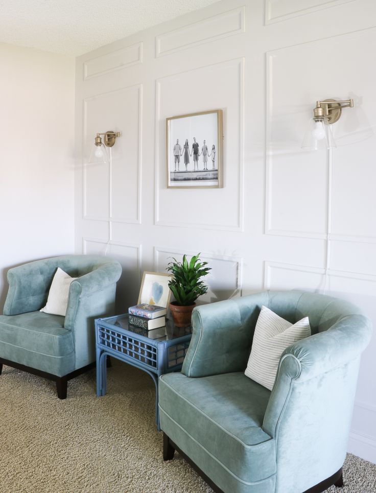 two chairs and a table in a room with white paneling on the wall behind them