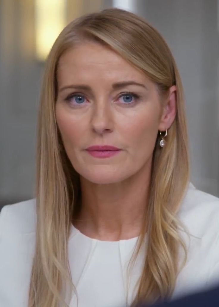 a woman with long blonde hair and blue eyes looks at the camera while wearing a white top