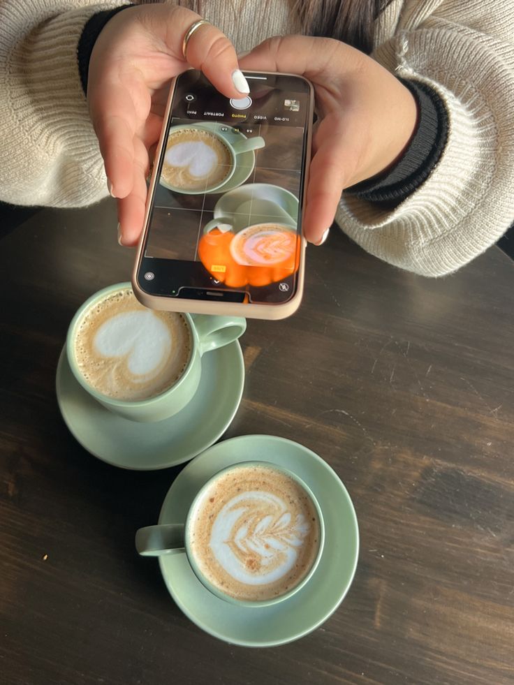 a person taking a photo of two cups of cappuccino with their cell phone