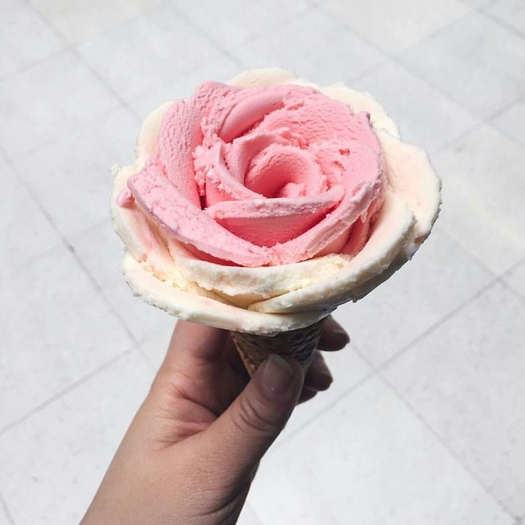 a hand holding an ice cream cone with pink frosting on it's top