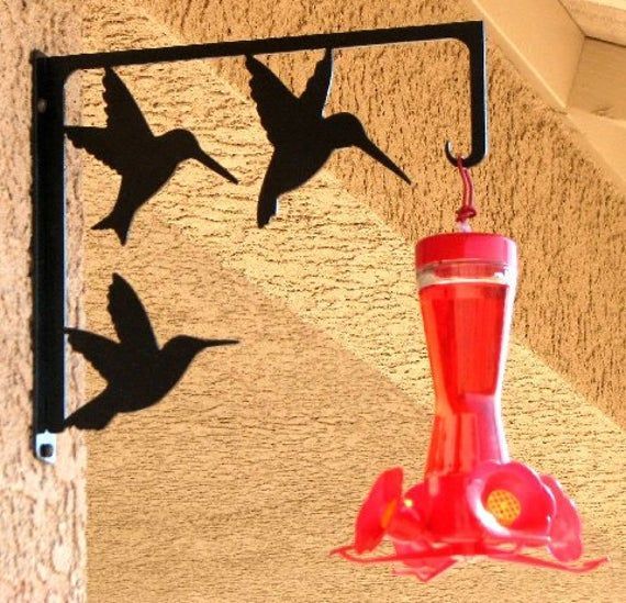 a red hummingbird feeder hanging from the side of a wall next to a window