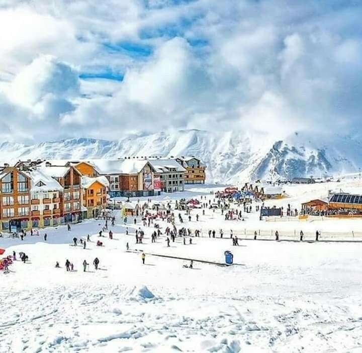 a group of people standing on top of a snow covered slope next to tall buildings