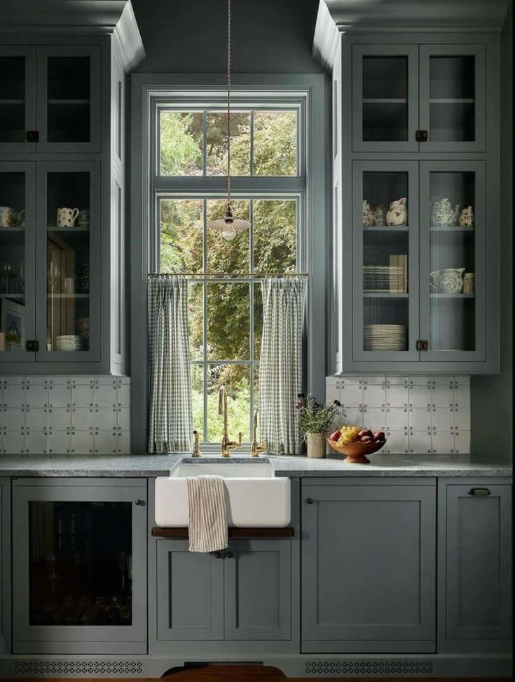 a kitchen with gray cabinets and white counter tops, along with a window over the sink