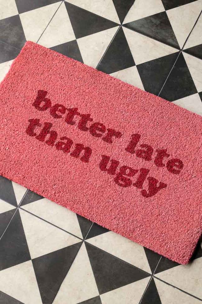 a pink door mat that says better late than ugly on the floor next to a black and white checkered floor