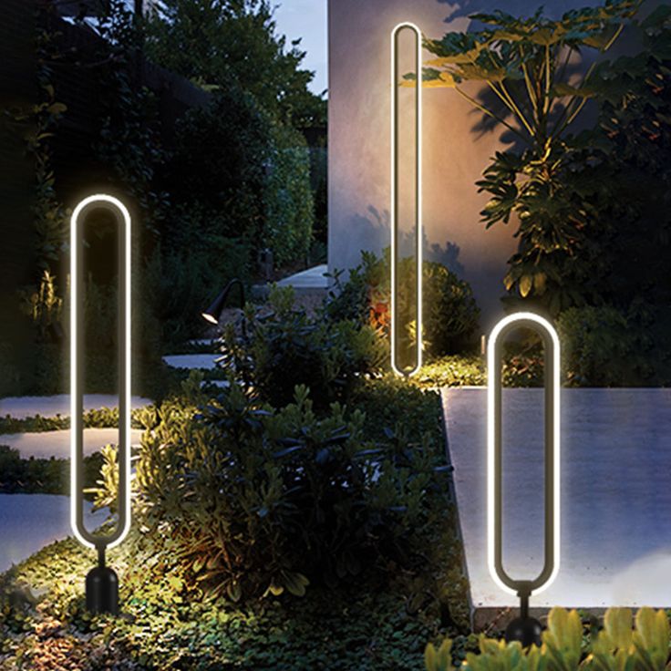 some lights that are in the grass near trees and bushes at night, with one light on