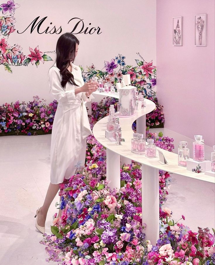 a woman standing in front of a table with perfume bottles on it and flowers all around