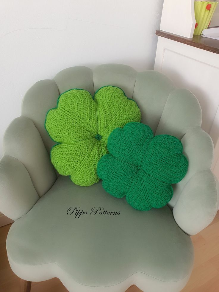 two green crocheted shamrocks sitting on top of a white chair in a room