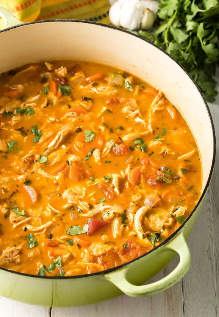 a green pot filled with chicken tortilla soup and garnished with cilantro