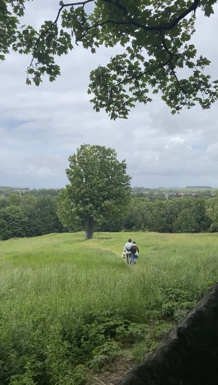 two people walking through a field with trees in the background