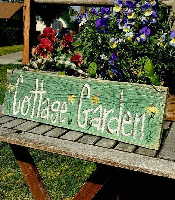 a wooden sign that says cottage garden with flowers in it on a picnic table outside