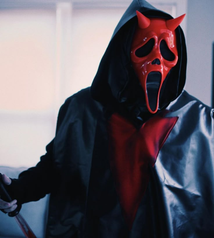 a man in a red devil mask and black jacket holding a knife with his mouth open