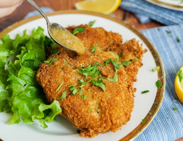 fried fish and greens on a plate with lemon wedges