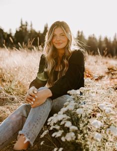 a woman sitting in the middle of a field with flowers on her knees and smiling