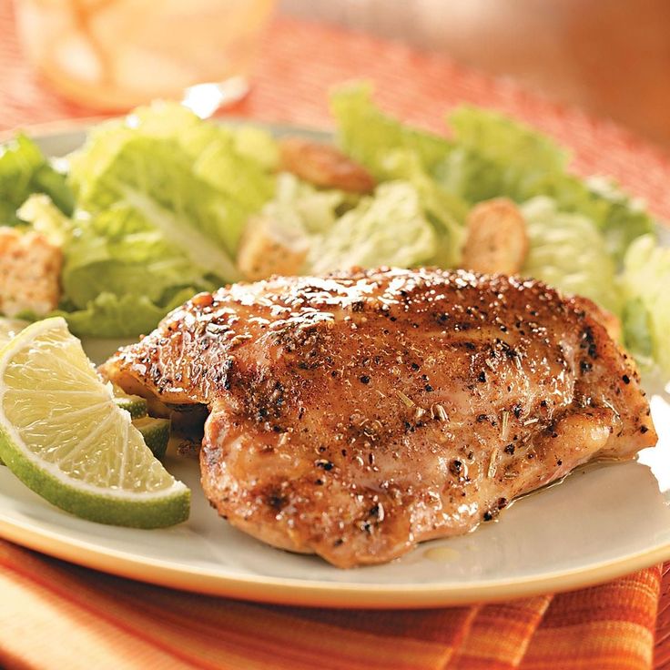 a white plate topped with meat, salad and lemon wedges on top of a table