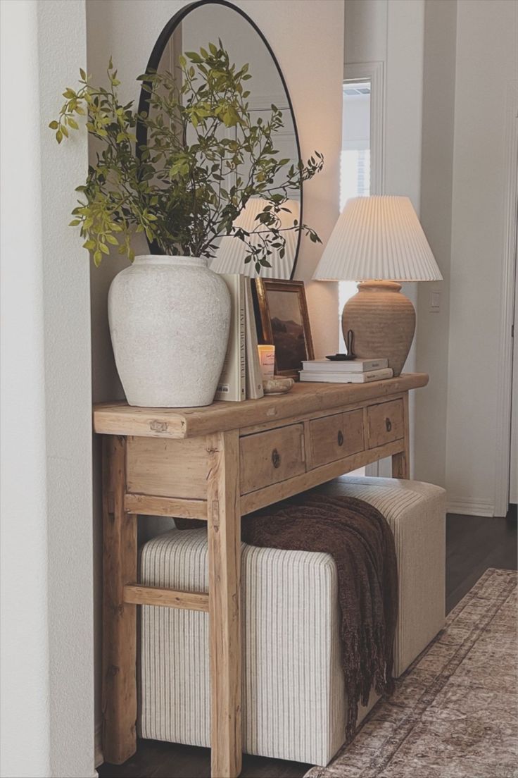 a wooden table topped with a white vase next to a mirror and plant on top of it