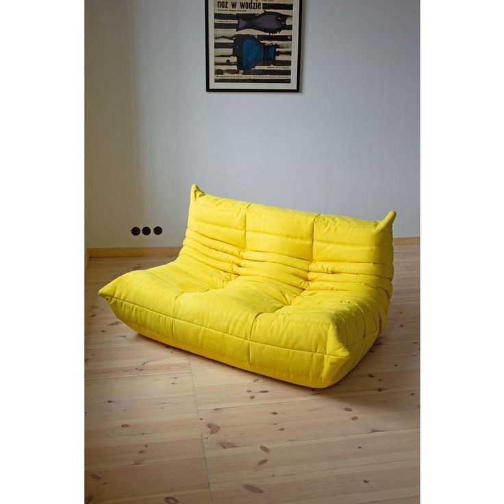 a yellow futon sofa sitting on top of a hard wood floor next to a painting