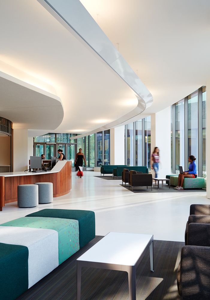 people are sitting in the lobby of an office building with high ceilings and floor to ceiling windows