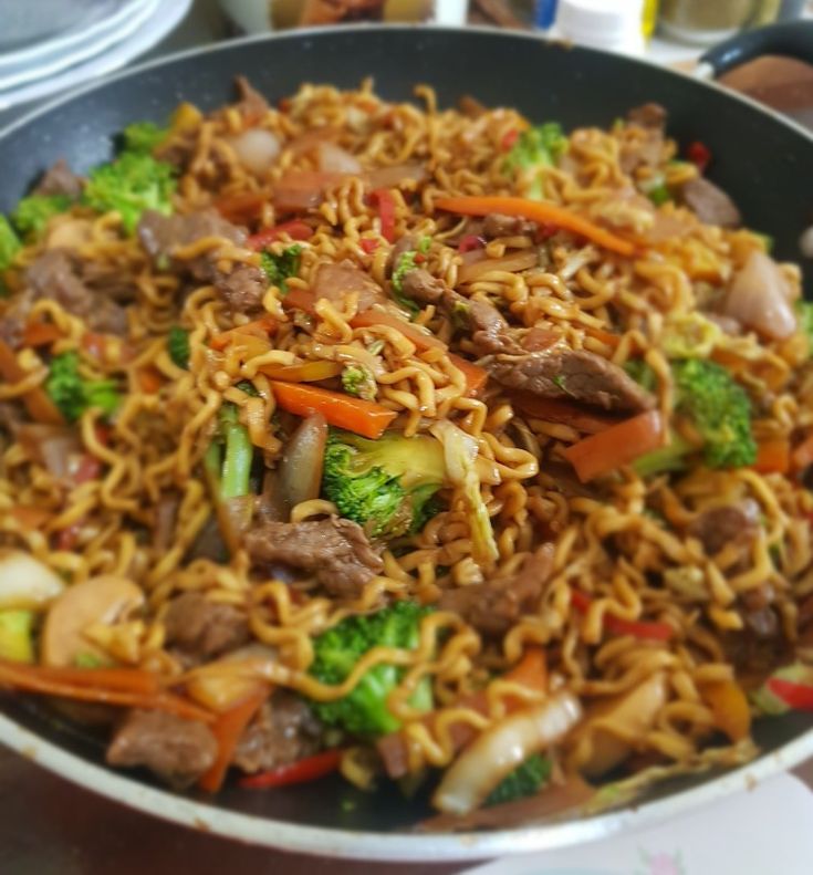 a pan filled with noodles, meat and veggies on top of a table